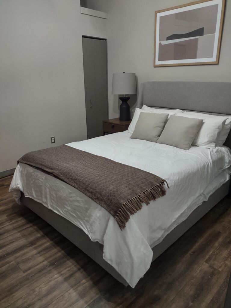 Freshly made bed in a clean bedroom with wood-look flooring