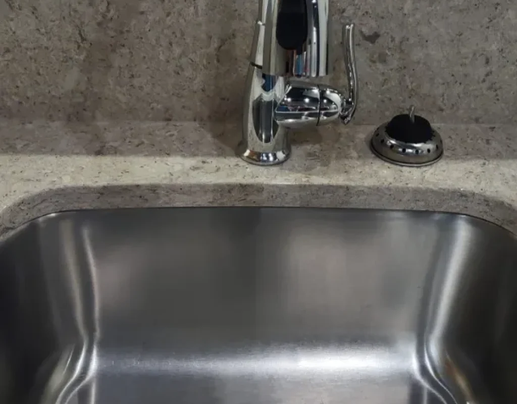 Polished stainless steel kitchen sink and faucet set in a stone countertop after a move out cleaning in Ralston, NE.